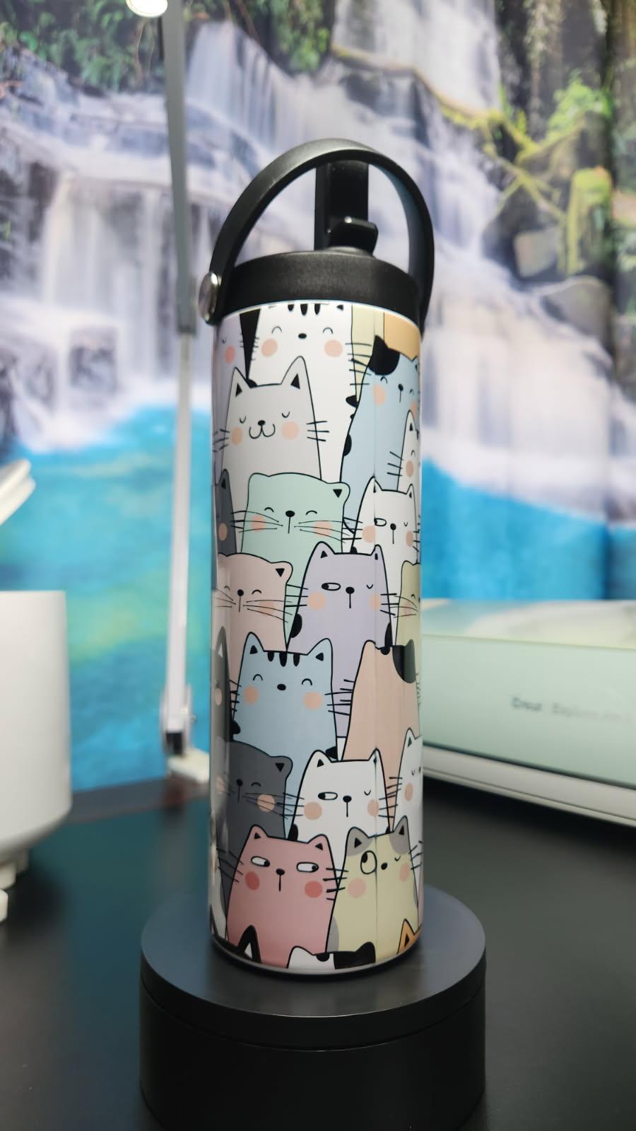 Thermos bottle with cat pattern on a black stand against a scenic background