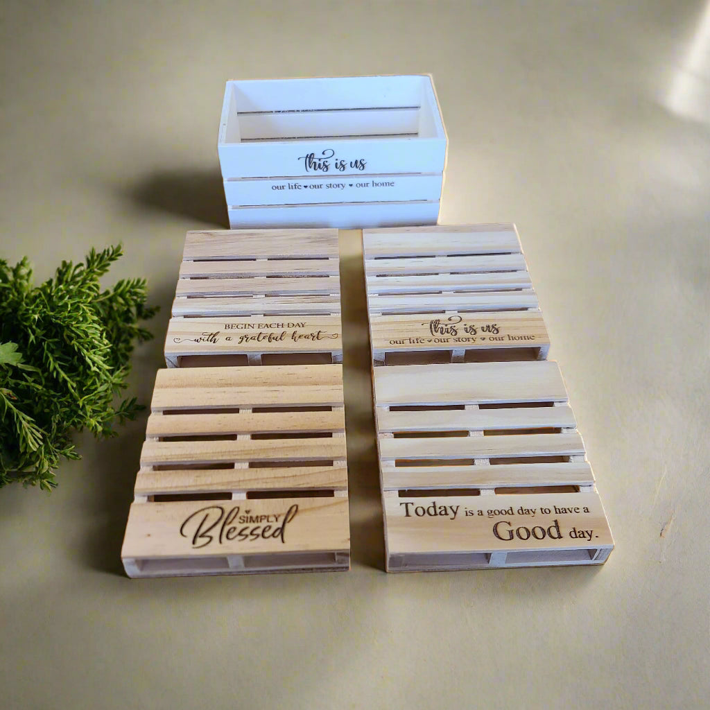 four pallet coasters with cork backing on a counter with a crate with the text 'this is us' etched into it. 