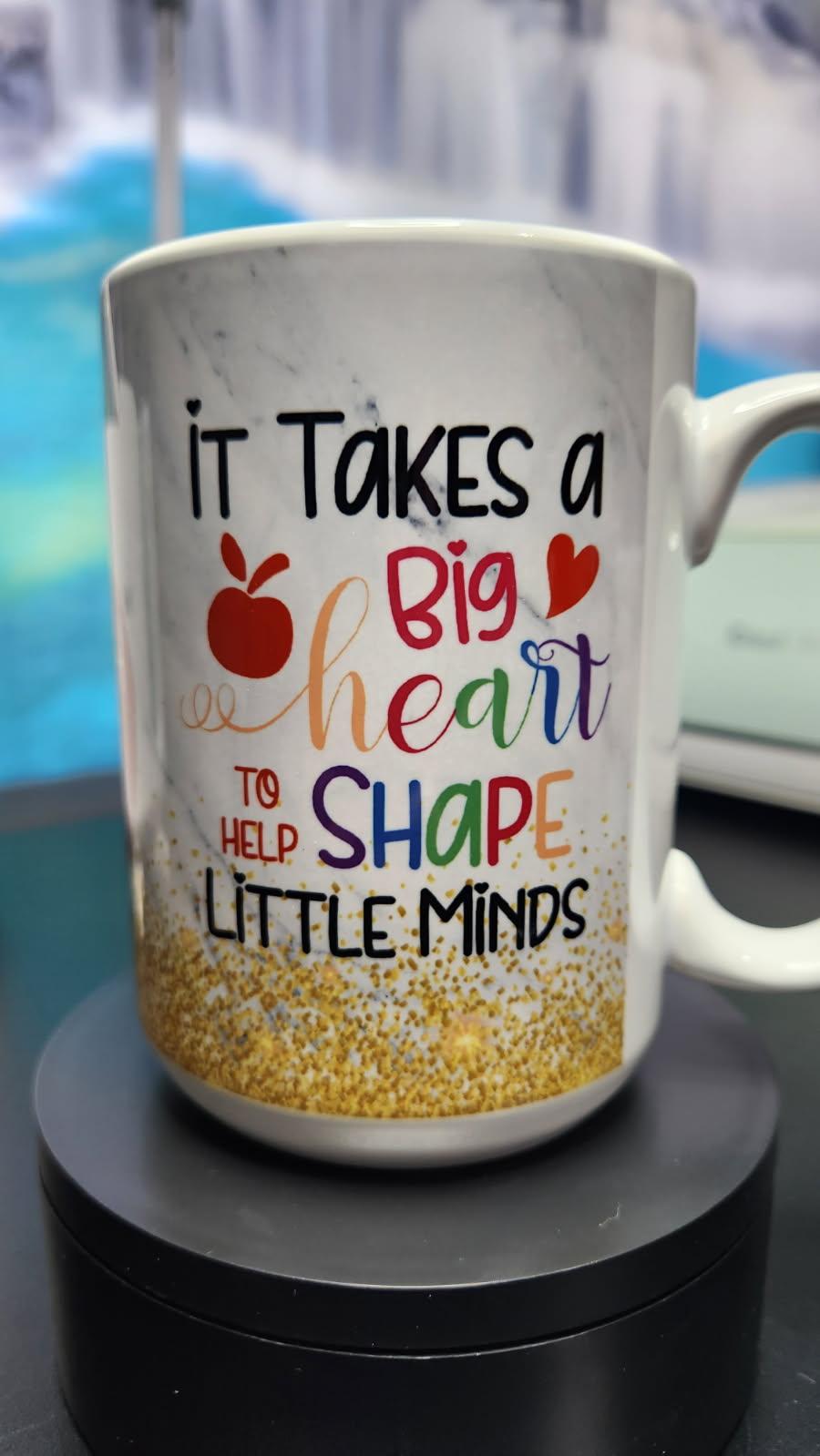Mug with motivational quote 'It takes a big heart to help shape little minds' on a blurred background