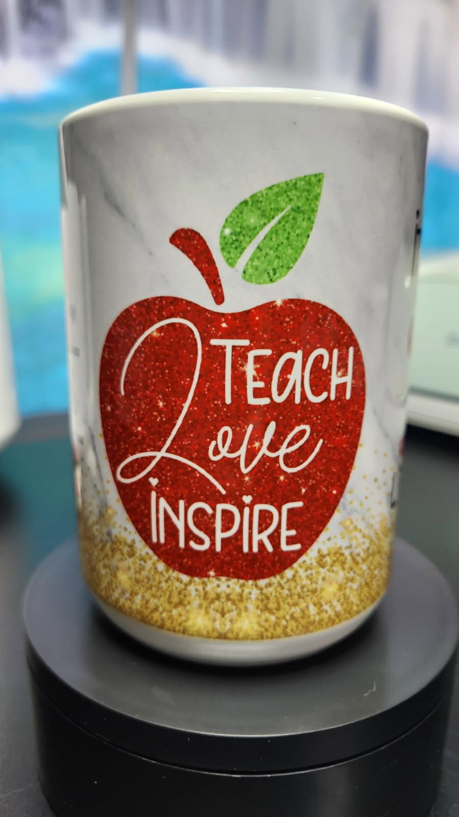 White mug with red apple design and text 'Teach Love Inspire' on a blurred background